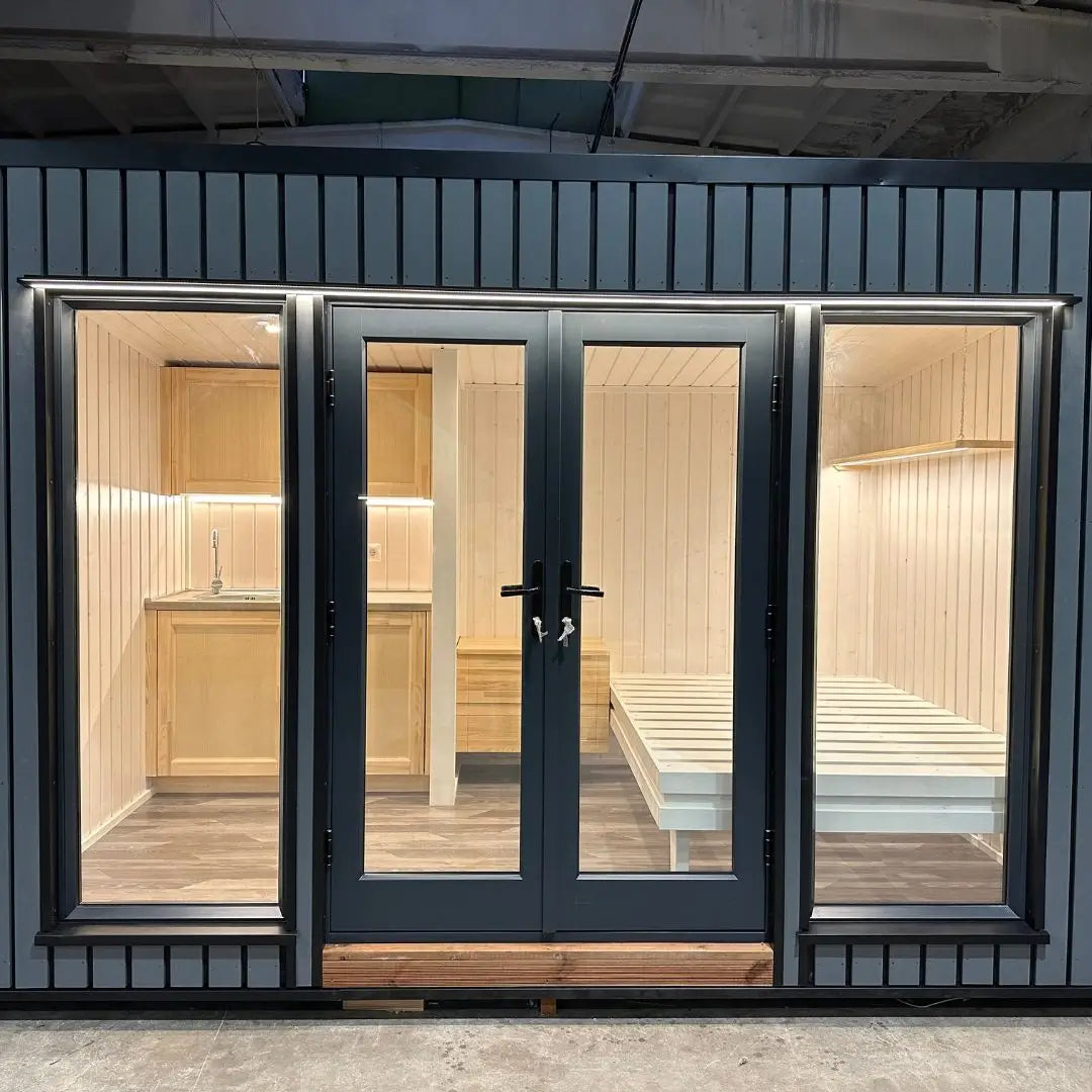 The Small GlampTainer container-style glamping structure – front view with full-glass doors revealing bright Scandi-style interior with kitchenette and bed frame.