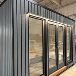 The Small GlampTainer container-style glamping structure – close-up of front façade with vertical timber cladding, glass doors and warm downlighting.