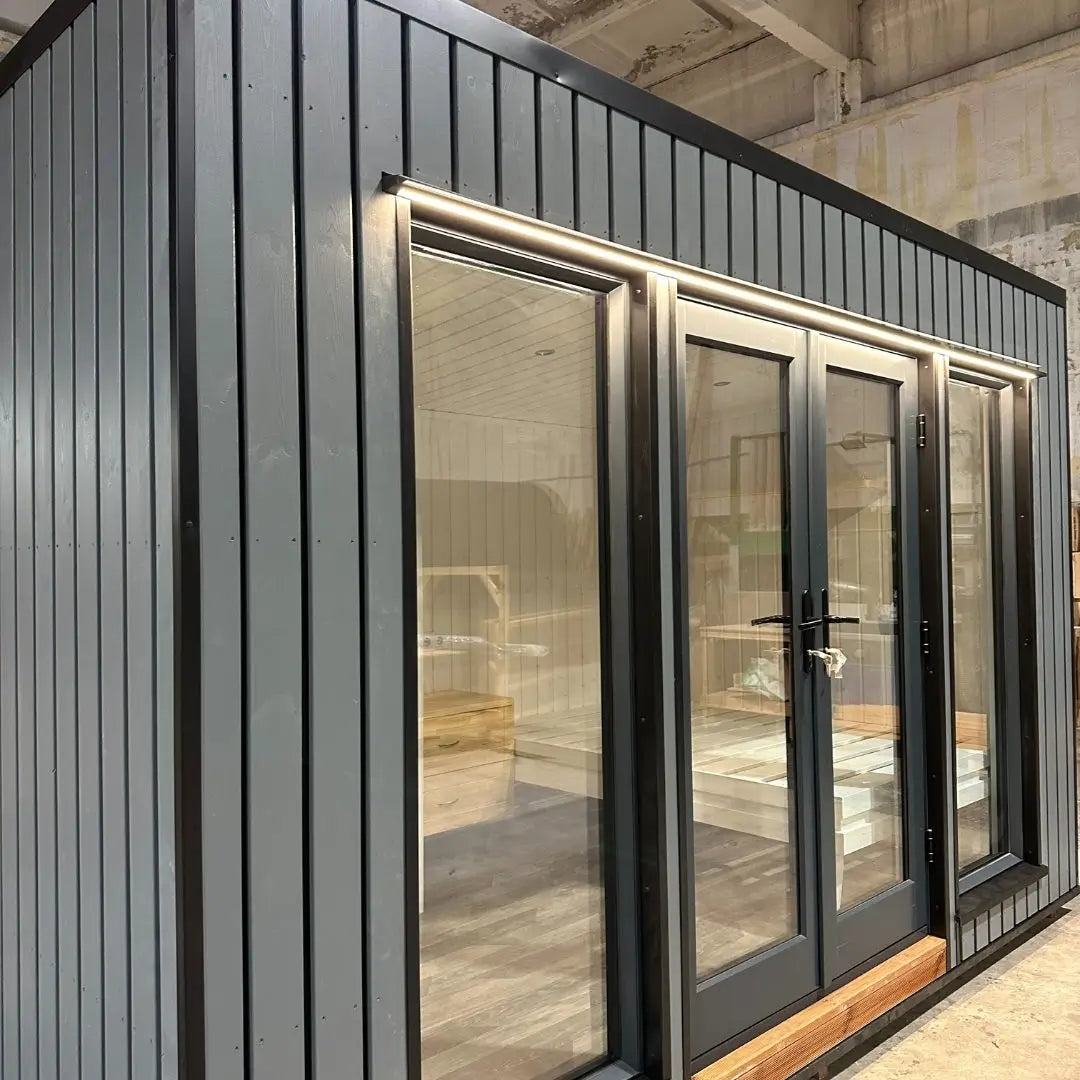 The Small GlampTainer container-style glamping structure – close-up of front façade with vertical timber cladding, glass doors and warm downlighting.