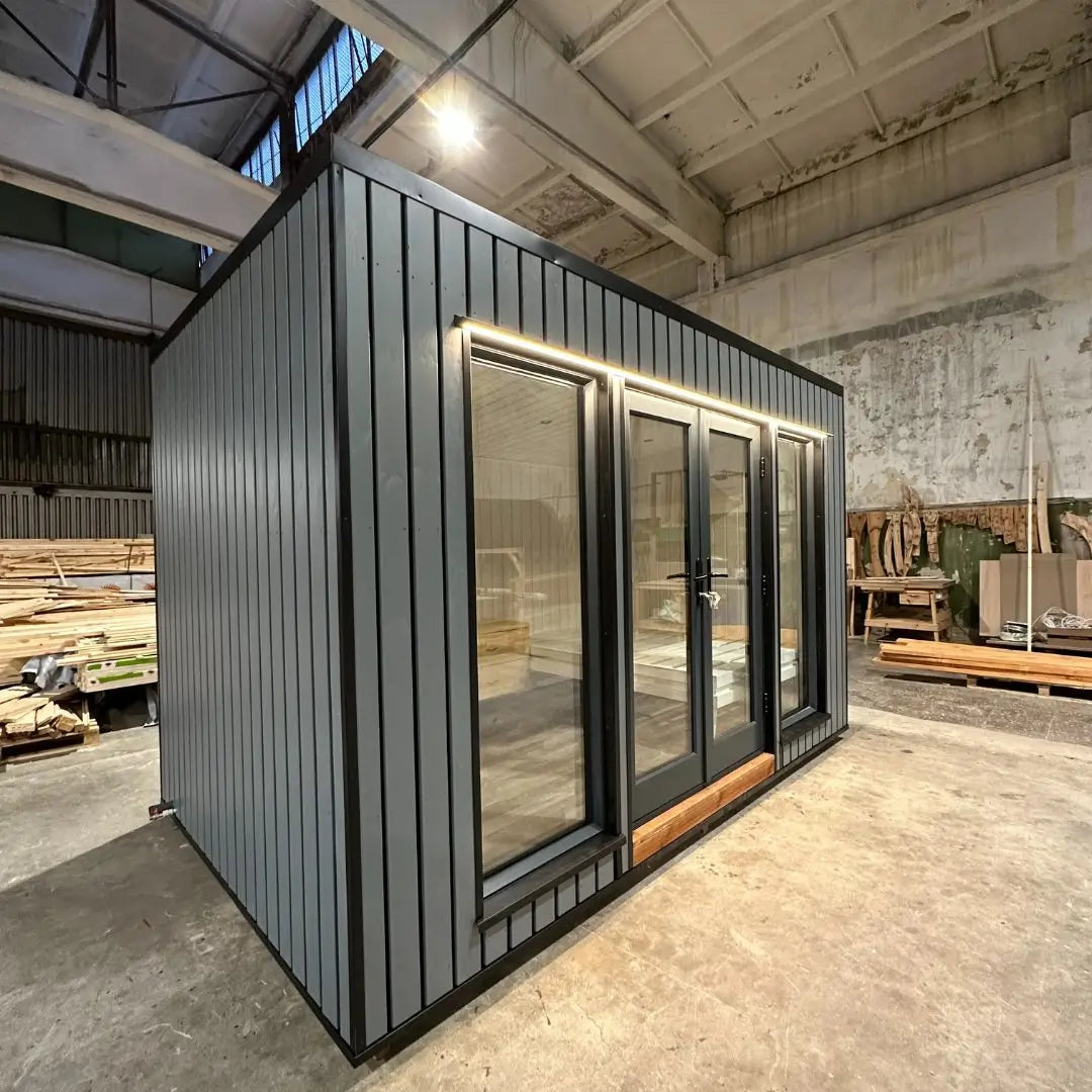 The Small GlampTainer container-style glamping structure – left side angle showing sleek dark-grey cladding, large glass panels and warm LED trim lighting.