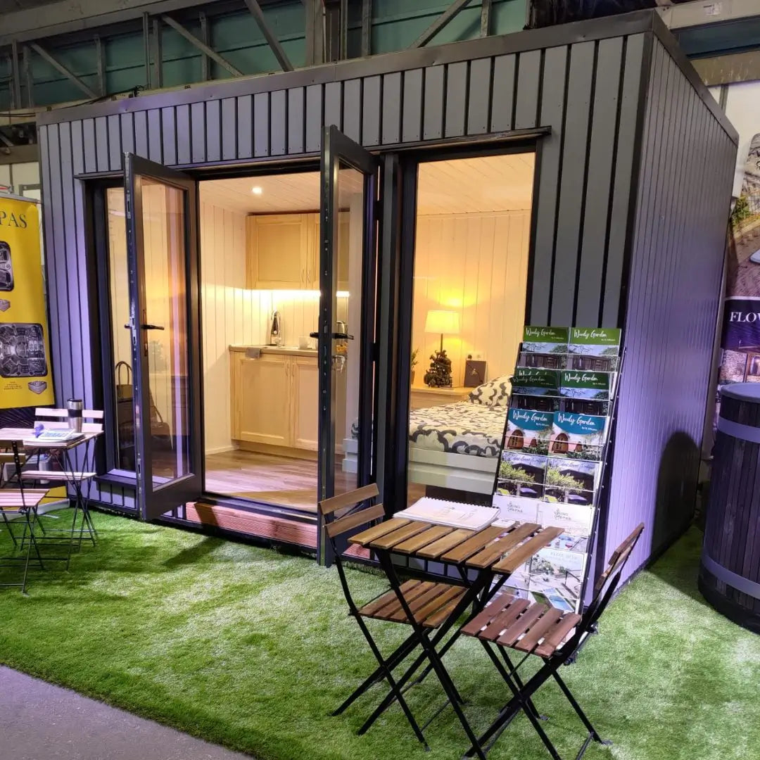 Fully furnished Small GlampTainer container-style glamping structure – showroom display with double bed, kitchenette, and outdoor bistro seating on artificial grass.