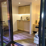 Compact kitchenette inside The Small GlampTainer container-style glamping structure – light wood cabinets, under-cabinet lighting and worktop with kettle and cups.