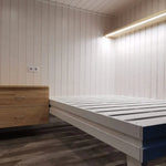 Minimalist sleeping nook in The Small GlampTainer container-style glamping structure – wooden nightstand and white bed frame against Scandi-style timber walls.