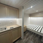 Compact interior of The Small GlampTainer container-style glamping structure – view from right side showing kitchenette, bed frame and warm downlighting.