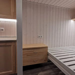 Functional interior of The Small GlampTainer container-style glamping structure – kitchen counter, wooden nightstand and bed frame under soft ceiling lights.