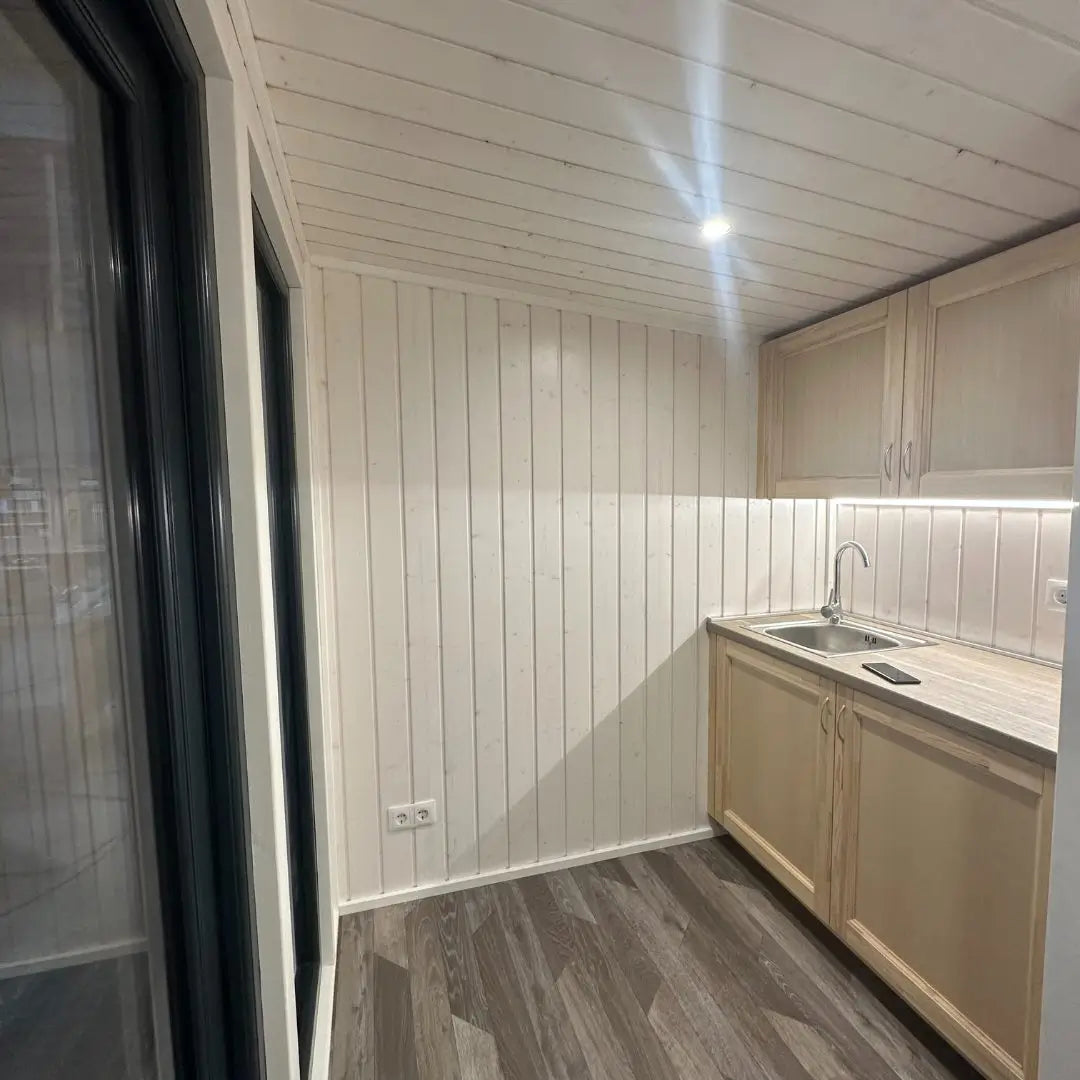 Side perspective of The Small GlampTainer container-style glamping structure – compact kitchenette with wood cabinets, integrated sink and under-lighting.