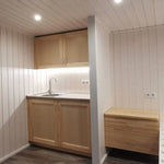 Minimalist kitchenette and nightstand inside The Small GlampTainer container-style glamping structure – light timber finishes with soft under-cabinet lighting.