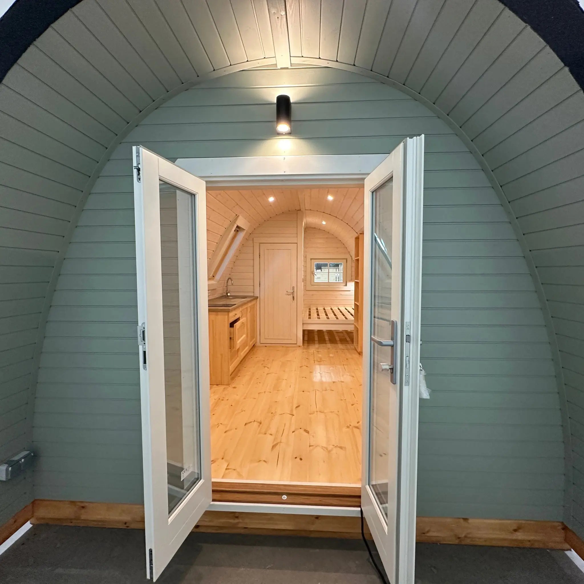 Front exterior view of The Twilight Pod with double doors open, revealing bright timber interior of luxury glamping pod
