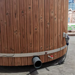 Exterior plumbing connections on The Washwood Barrel showing water inlet and drainage outlets.