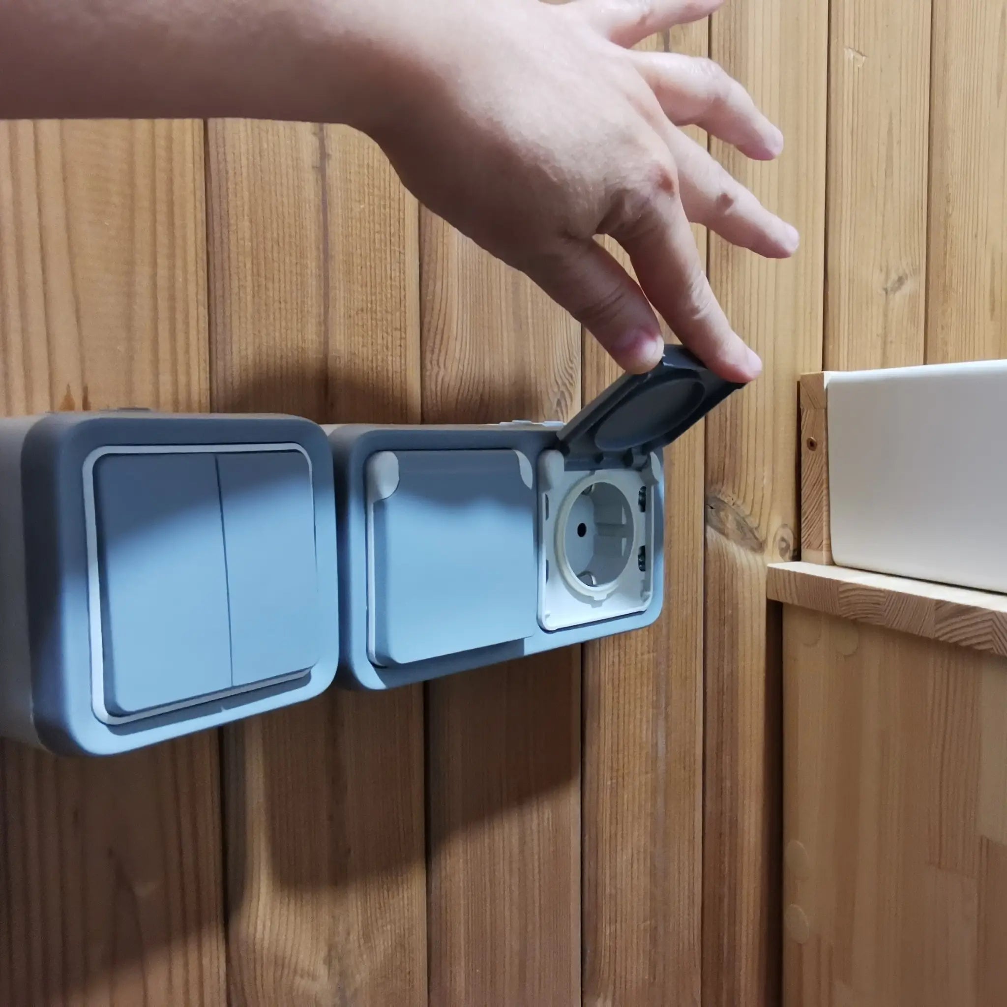 Interior wall-mounted electrical socket inside The Washwood Barrel with protective weatherproof cover open.