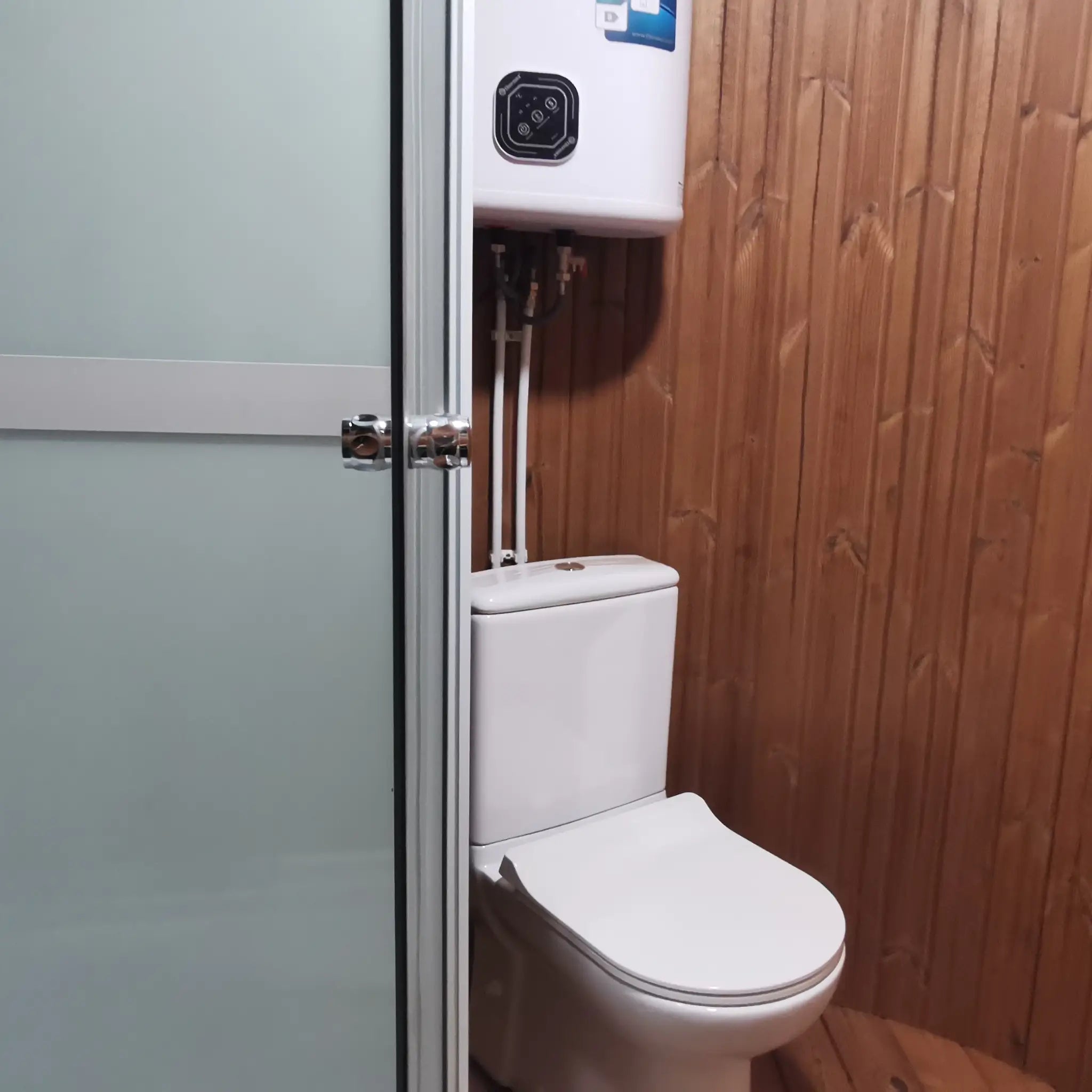 Partial view of toilet behind shower enclosure with water heater above in Washwood Barrel