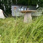 Rustic shepherd’s hut nestled in tall grass with outdoor dining table and woodland surroundings for a tranquil countryside retreat.