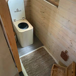 Compact wooden bathroom interior with eco-friendly compost toilet, woven rug, and natural rustic finishes.