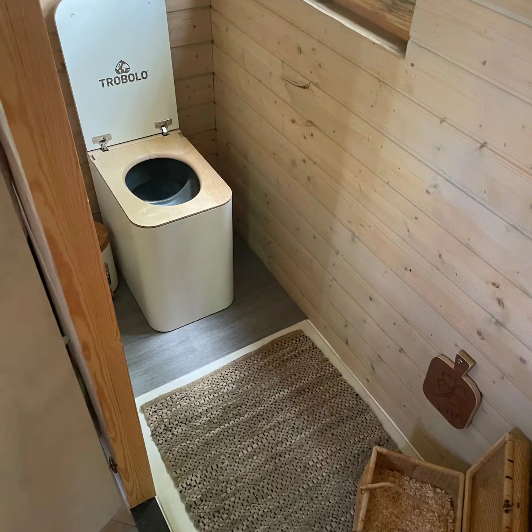 Compact wooden bathroom interior with eco-friendly compost toilet, woven rug, and natural rustic finishes.