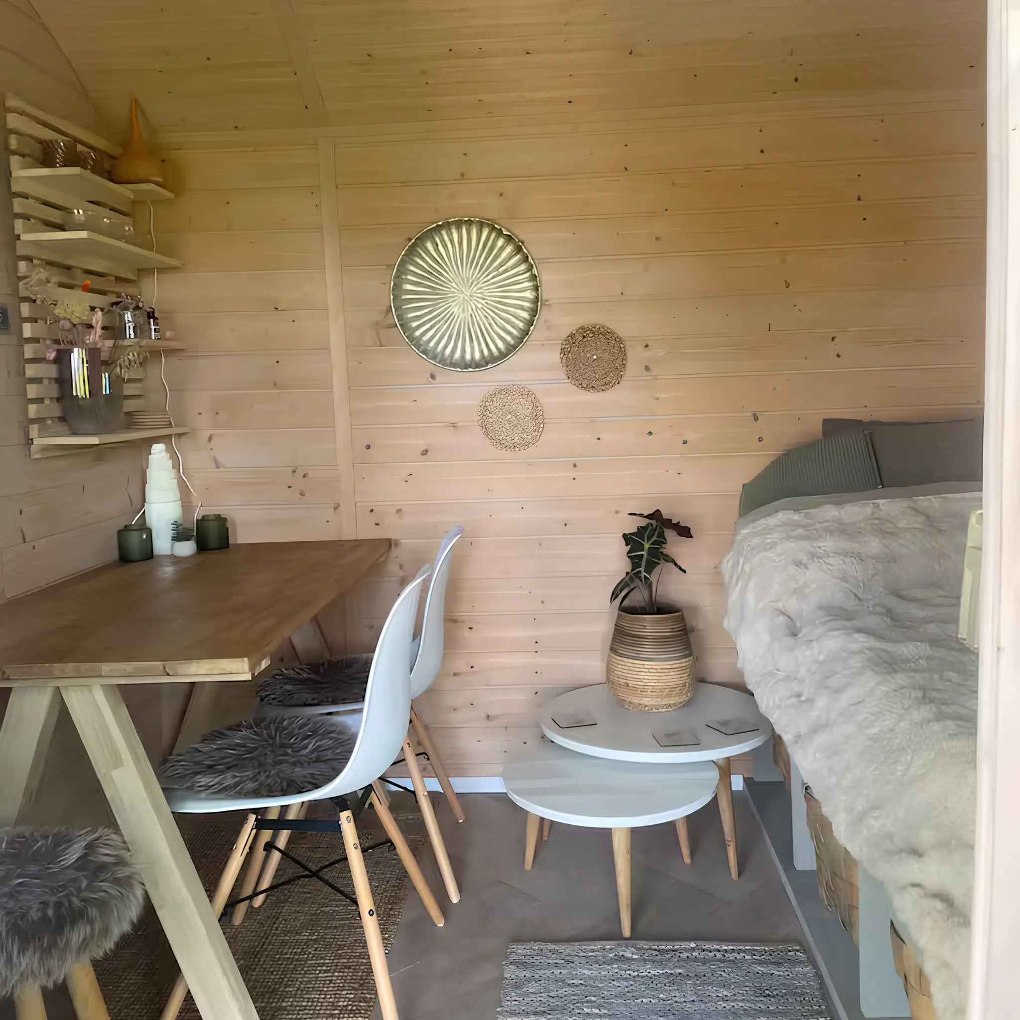 Open-plan shepherd’s hut interior featuring dining area, cosy sleeping space, wooden décor, and soft neutral styling.