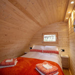 Comfortable double bedroom in The Dual Halfmoon luxury 4 person glamping pod with timber walls, reading lights and feature window
