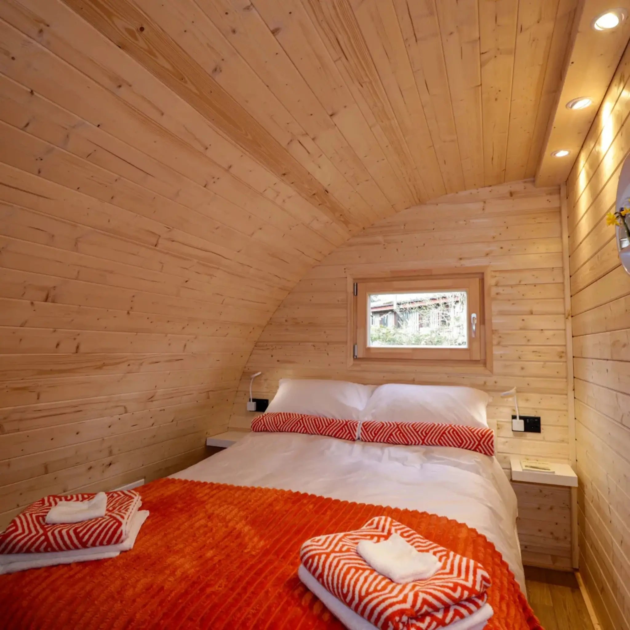 Comfortable double bedroom in The Dual Halfmoon luxury 4 person glamping pod with timber walls, reading lights and feature window