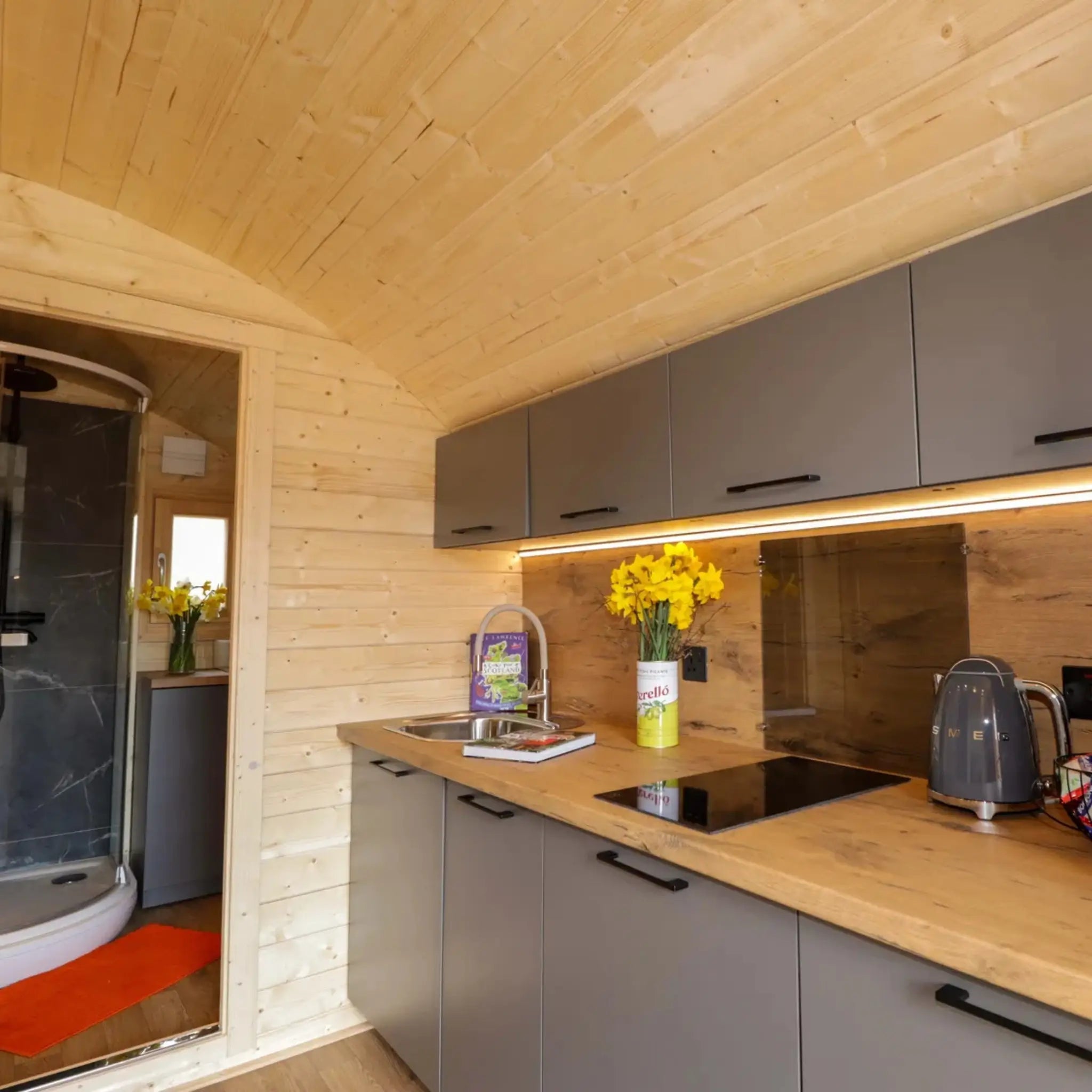 Open-plan kitchenette leading to the bathroom inside The Dual Halfmoon luxury 4 person glamping pod with modern fitted interior