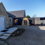 Wide front view of Hobbit garden office pod in landscaped garden setting with gravel courtyard and contemporary home backdrop