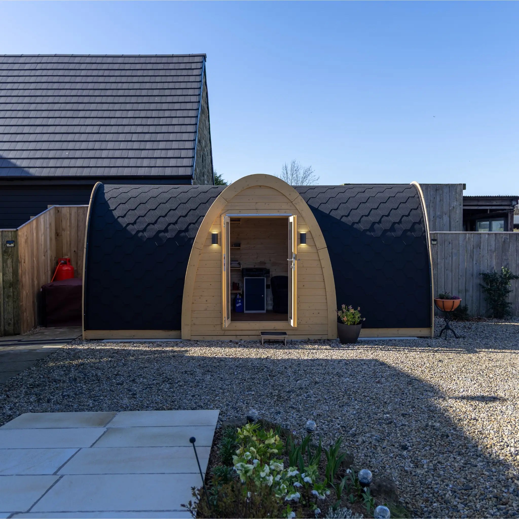 Luxury Hobbit garden office pod exterior front view with double doors, curved timber frame and black shingle roof in modern backyard