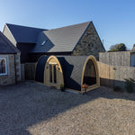 Wide garden perspective of Hobbit garden pod showing unique arched structure, black shingle roof and premium outdoor office setup