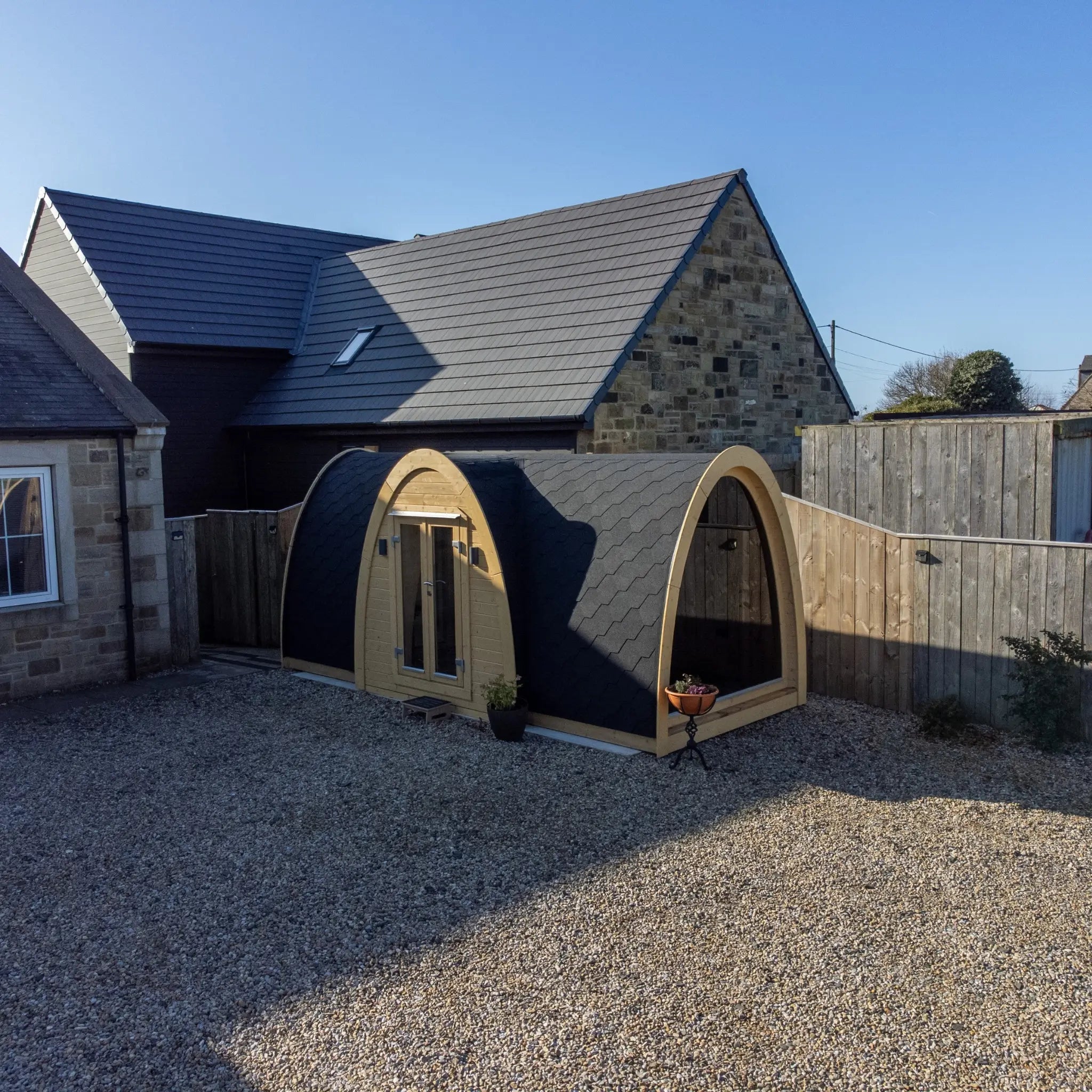 Wide garden perspective of Hobbit garden pod showing unique arched structure, black shingle roof and premium outdoor office setup