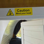Safety sign “Caution Mind Your Head” above bathroom door inside compact Hobbit pod interior