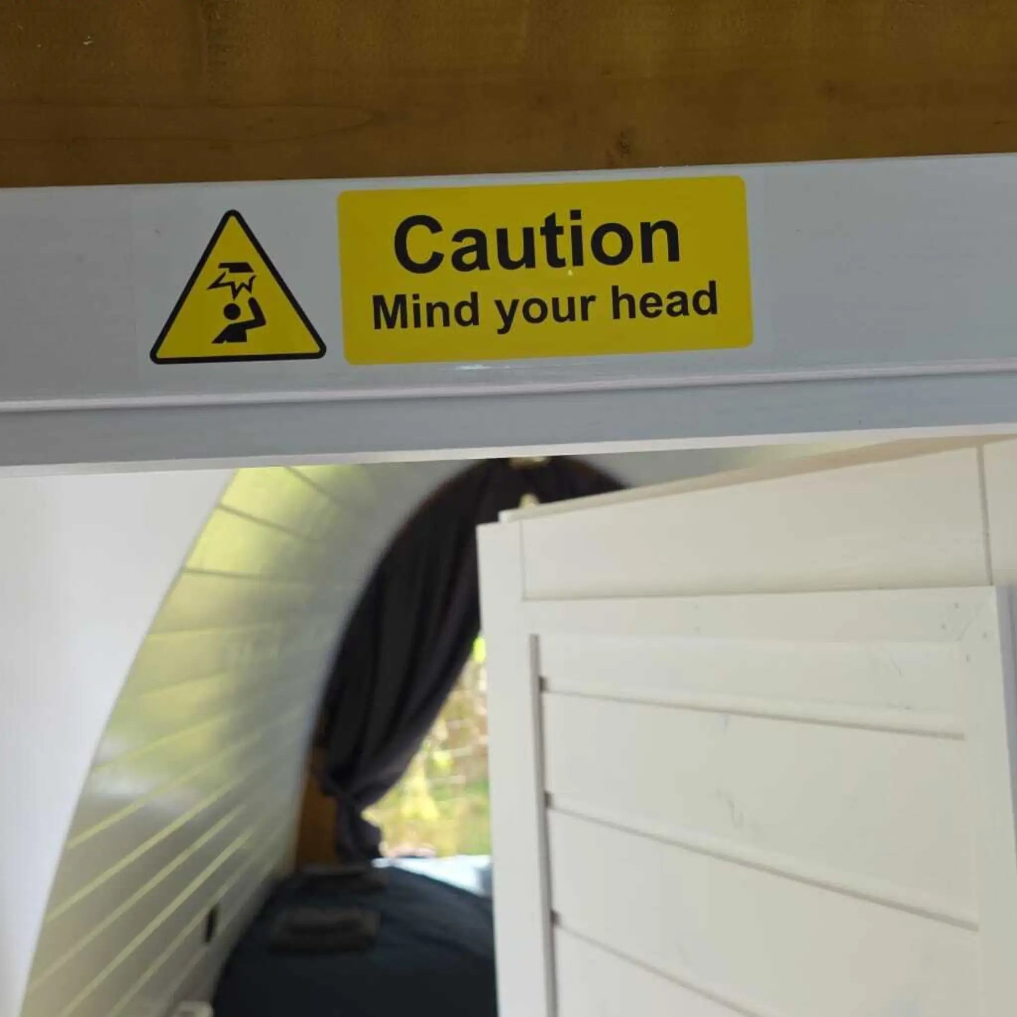 Safety sign “Caution Mind Your Head” above bathroom door inside compact Hobbit pod interior