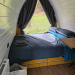 Wide view of Hobbit pod bedroom with double bed, large window and natural light overlooking outdoors