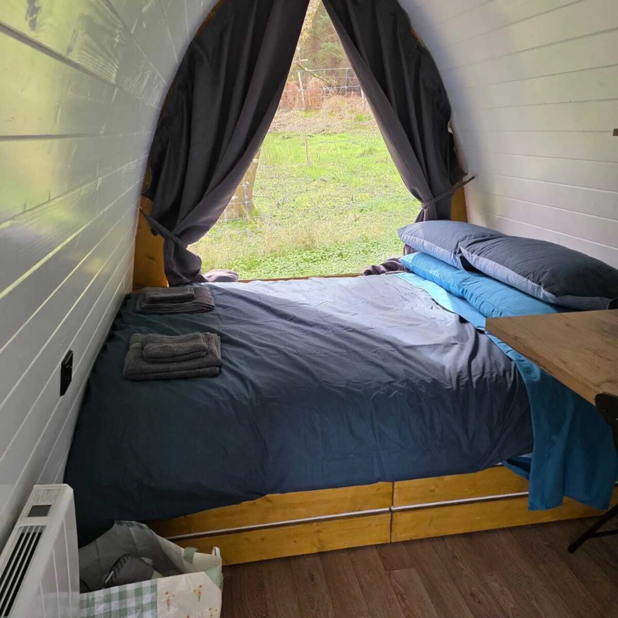 Wide view of Hobbit pod bedroom with double bed, large window and natural light overlooking outdoors