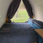 Cosy sleeping area inside Hobbit pod with bed next to full glass wall and countryside view