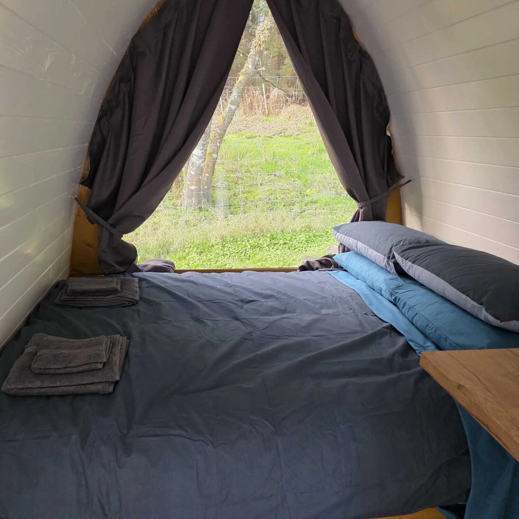 Cosy sleeping area inside Hobbit pod with bed next to full glass wall and countryside view