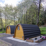 Rear view of two timber glamping pods with black curved roofs