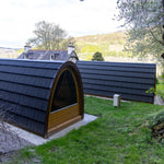 Side view of luxury Hobbit glamping pods with panoramic glazed end walls in a woodland setting