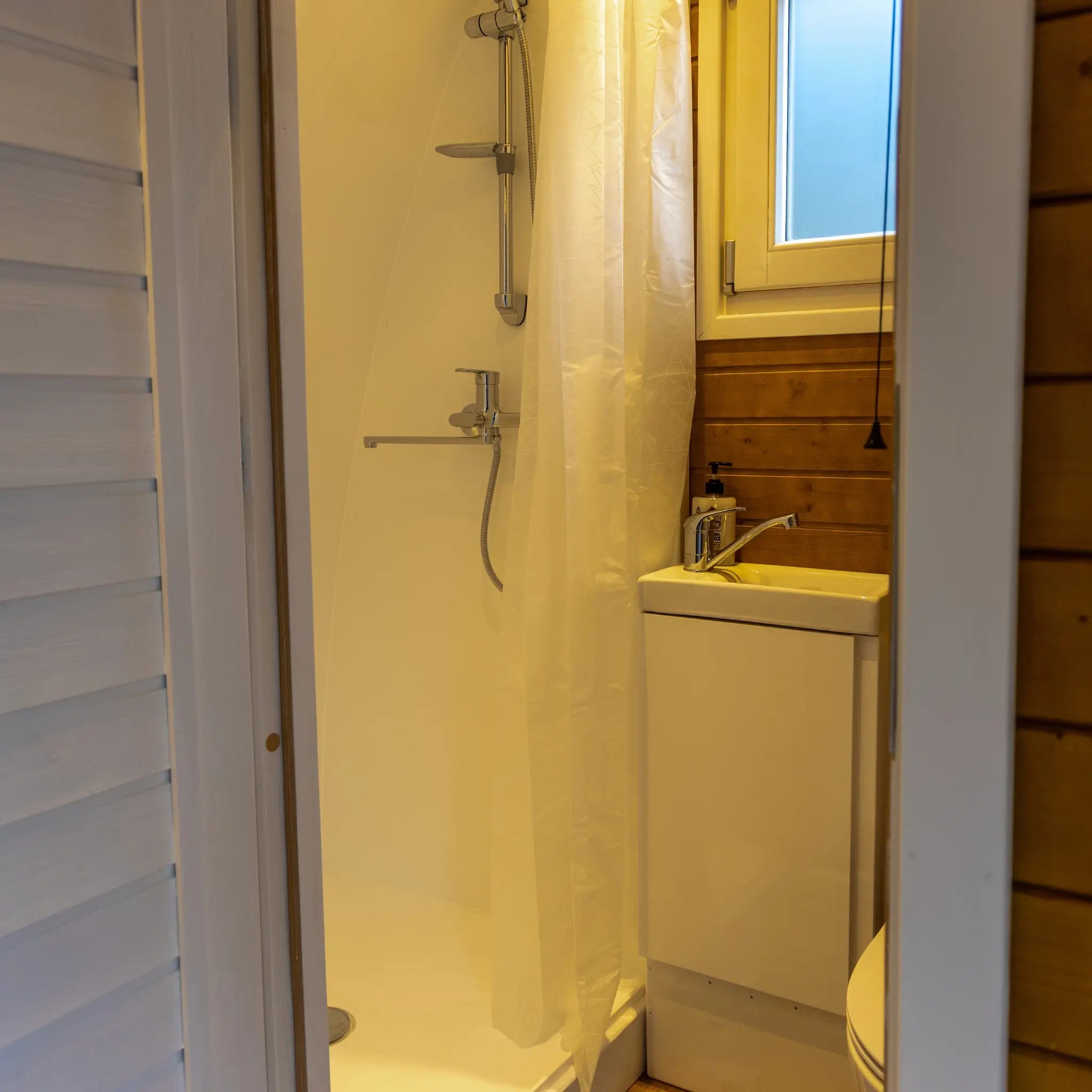 Compact ensuite bathroom with shower, sink and window inside glamping pod