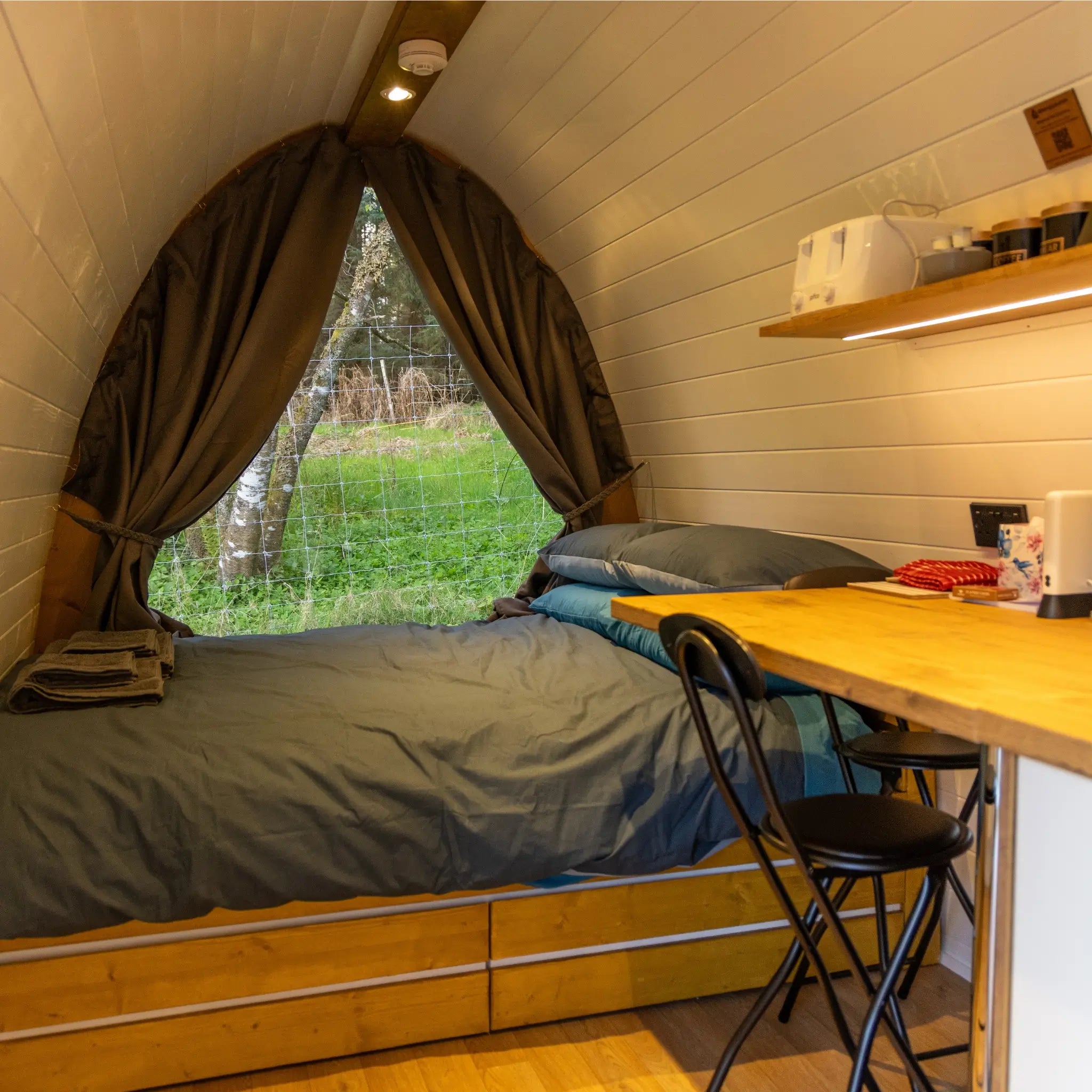 Interior of luxury glamping pod with double bed, desk and panoramic rear window