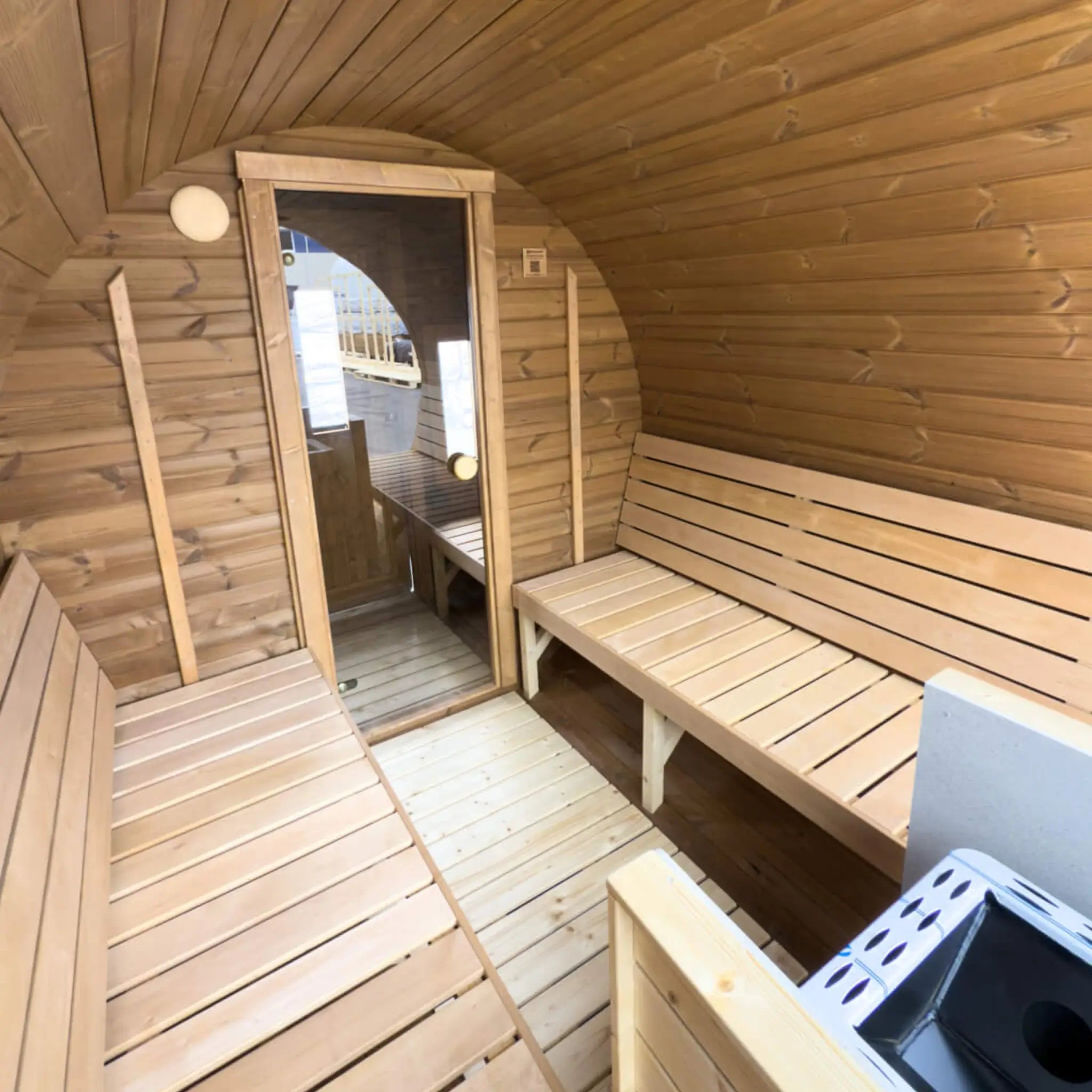 Spacious barrel sauna interior with wood-burning heater and bench seating for up to eight people