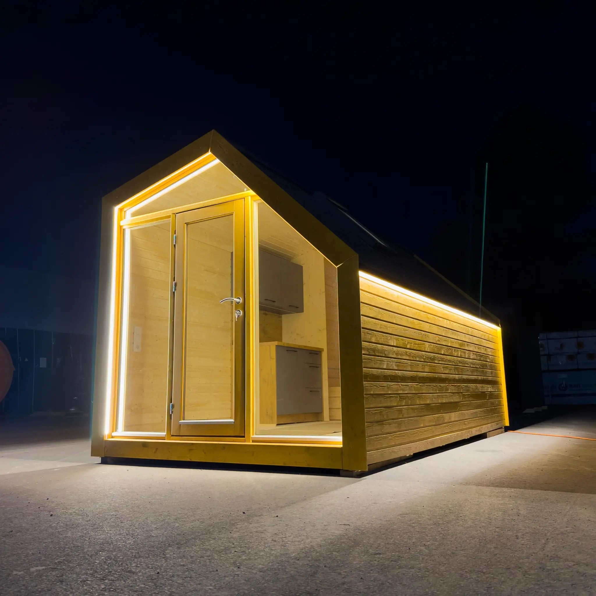 Night-time exterior view of The Ridgefall Pod, a 2 person glamping pod illuminated with integrated LED lighting and a modern pitched roof design.