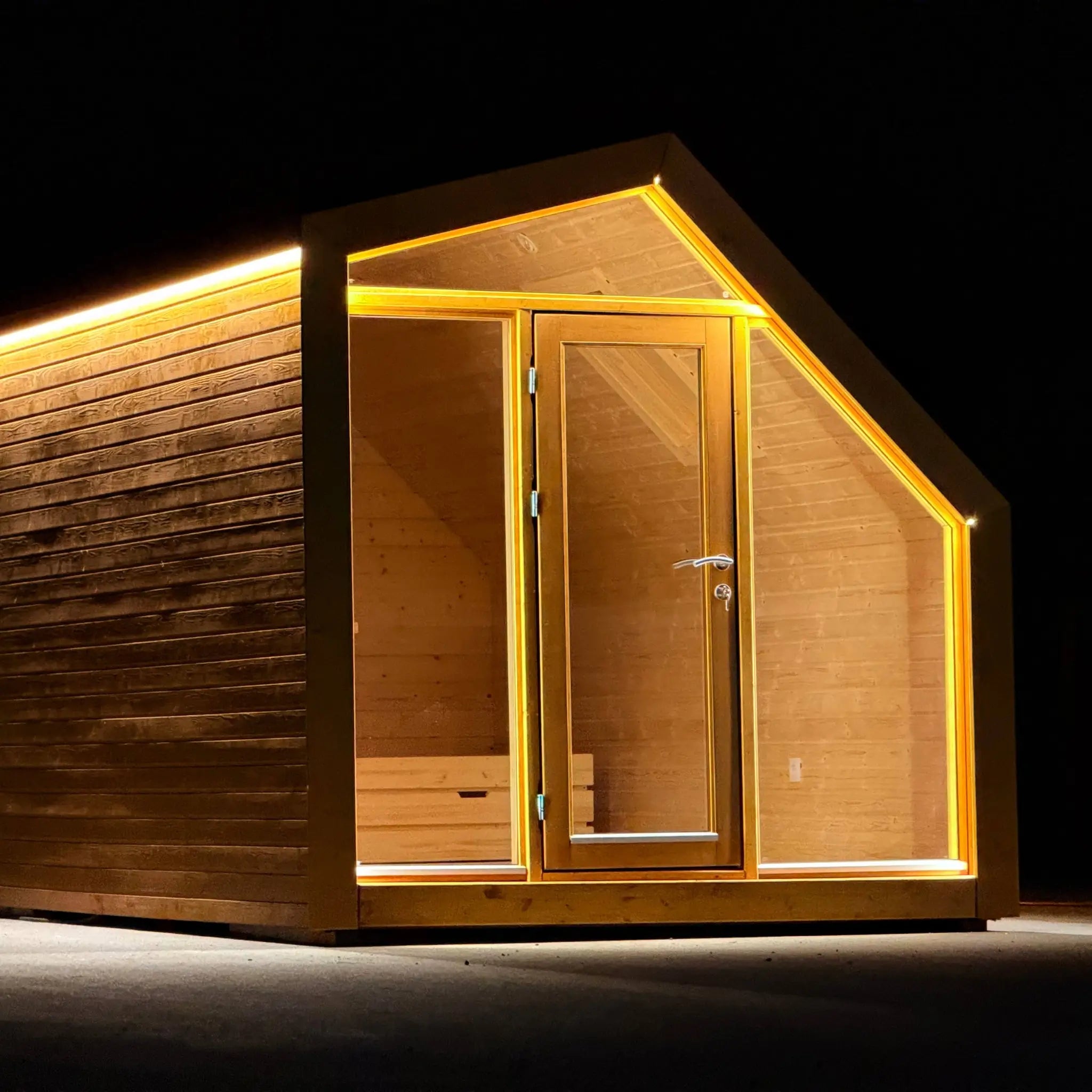 Front exterior night view of The Ridgefall Pod, showcasing LED-lit glazing, timber cladding, and compact luxury glamping design.
