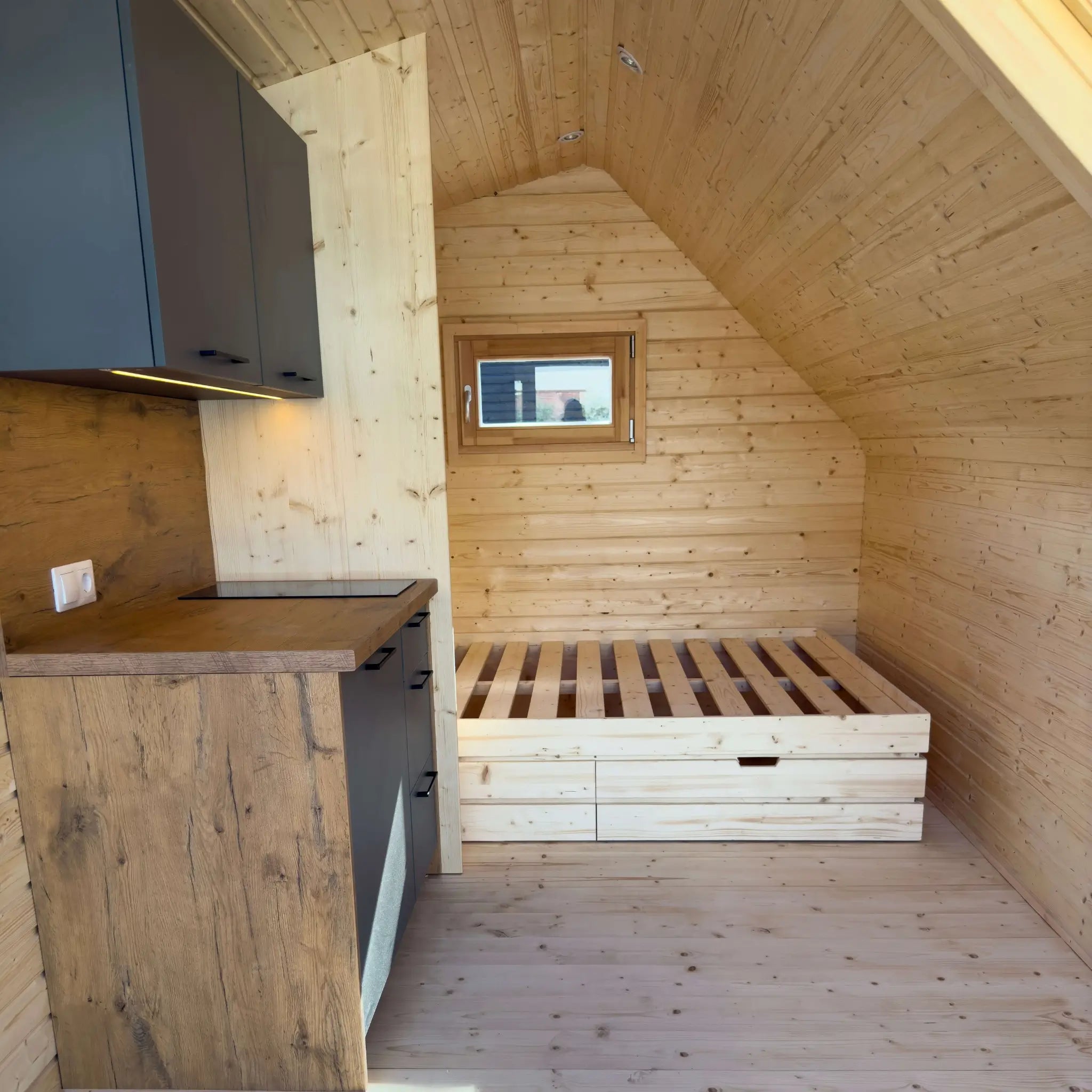 Open-plan interior of The Ridgefall Pod 2 person glamping pod showing the kitchenette and raised bed platform.