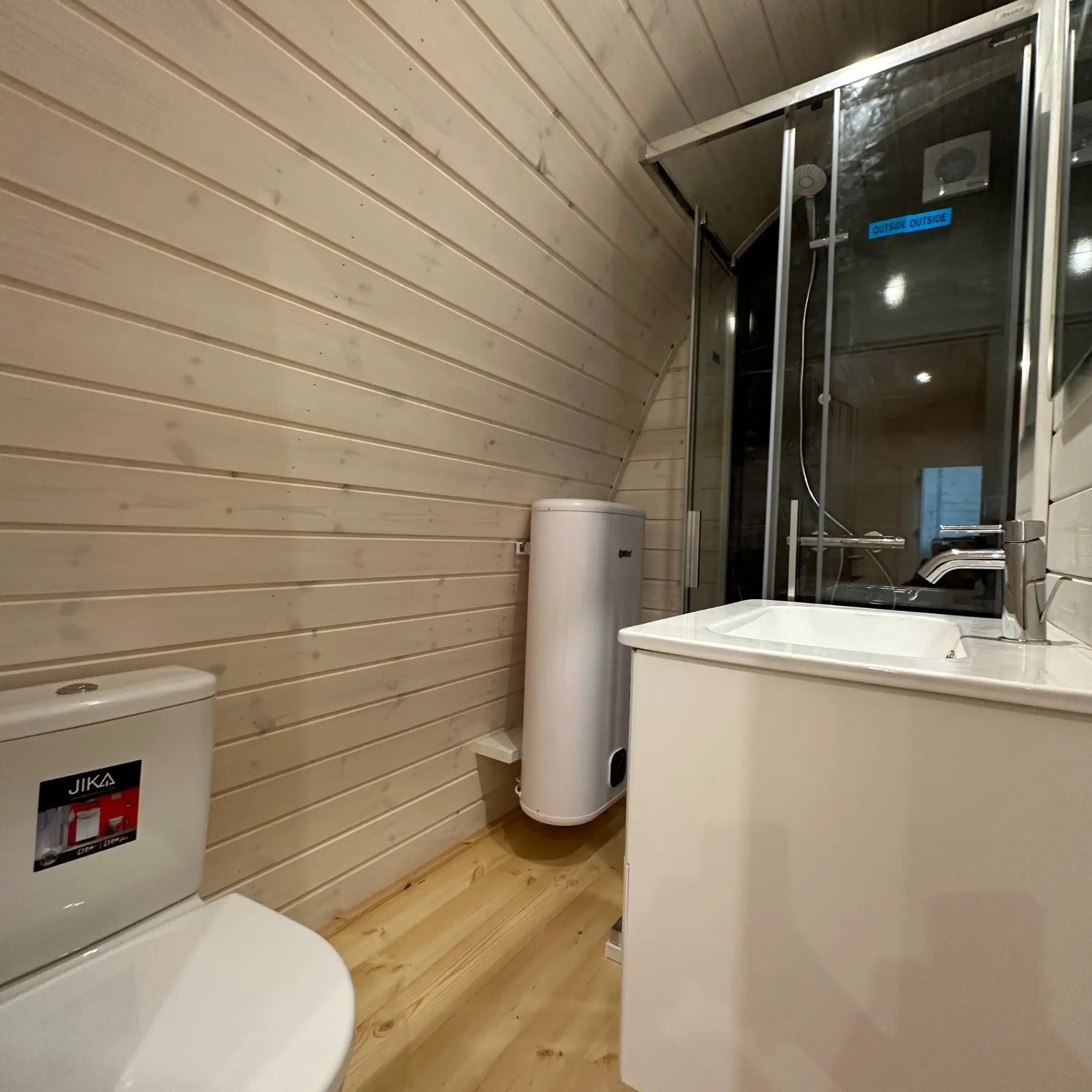 Angled interior view of the compact bathroom inside The Twilight Pod featuring shower enclosure, toilet, and water heater