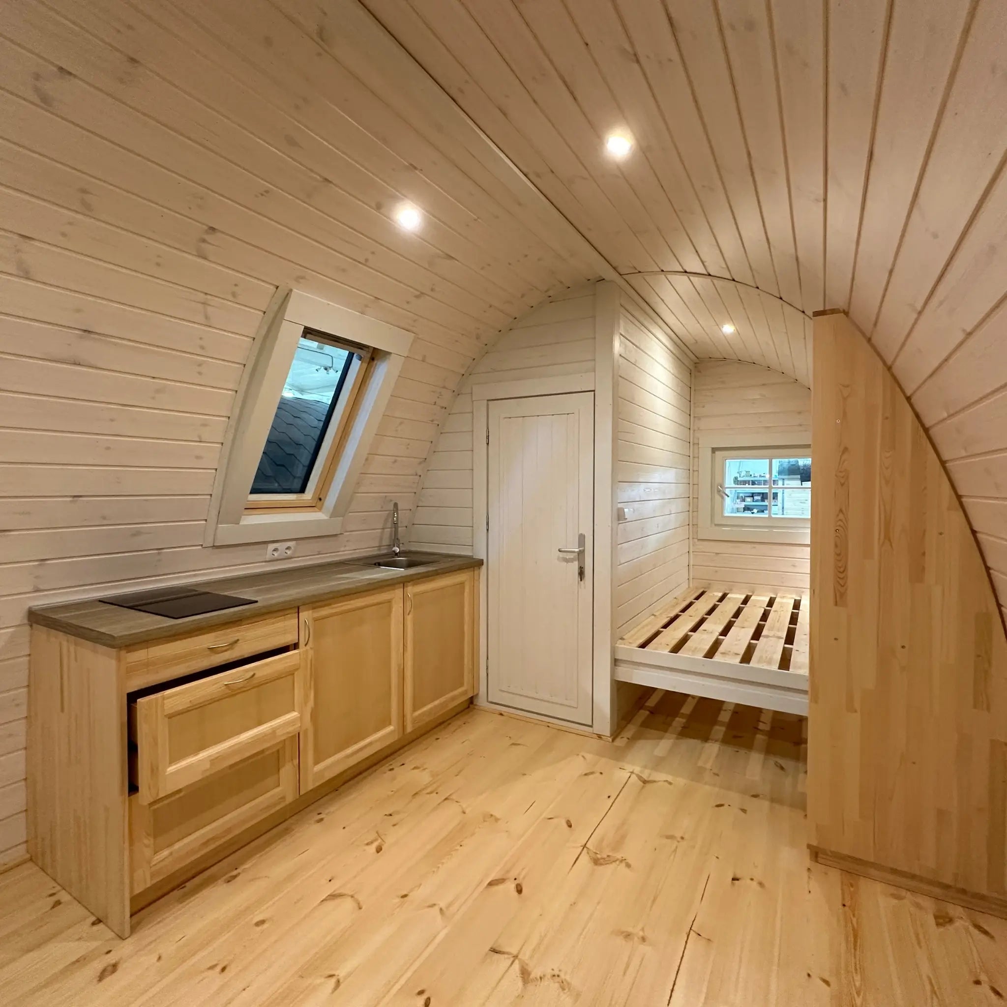 Wide interior view of The Twilight Pod displaying kitchenette, bathroom door, and sleeping area layout