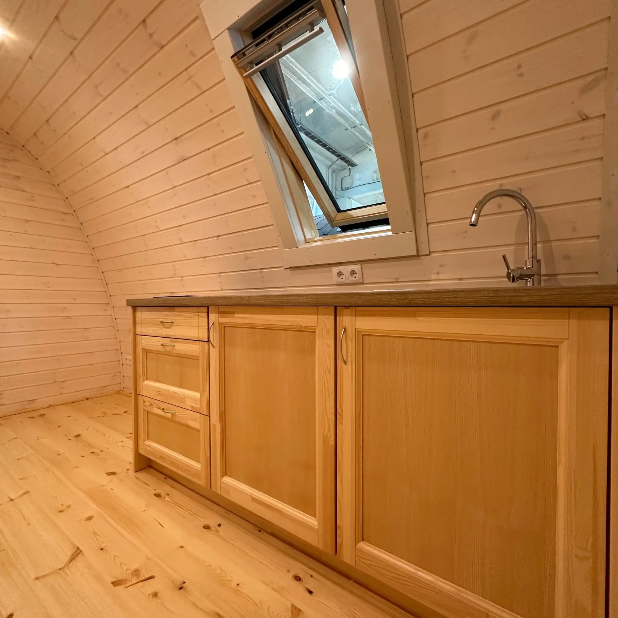 Open living space with fitted kitchen units and curved timber interior inside the Twilight luxury glamping pod