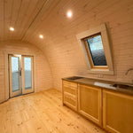 Open-plan interior layout showing kitchen counter, timber walls, and entrance doors in the Twilight glamping pod