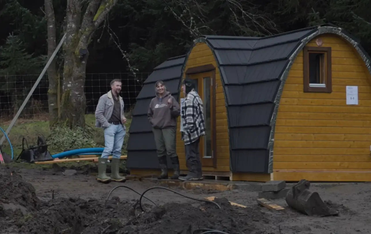 Taylor Glass standing with Doune House Pods owners Nigel and Mags Andrews beside newly installed glamping pods during a site visit in the Scottish Highlands.