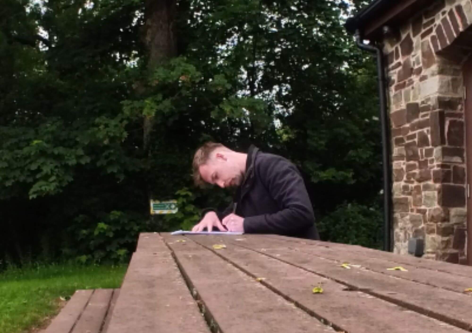 Taylor Glass founder of GlampLaunch sitting outdoors at a wooden table reviewing paperwork and making notes.