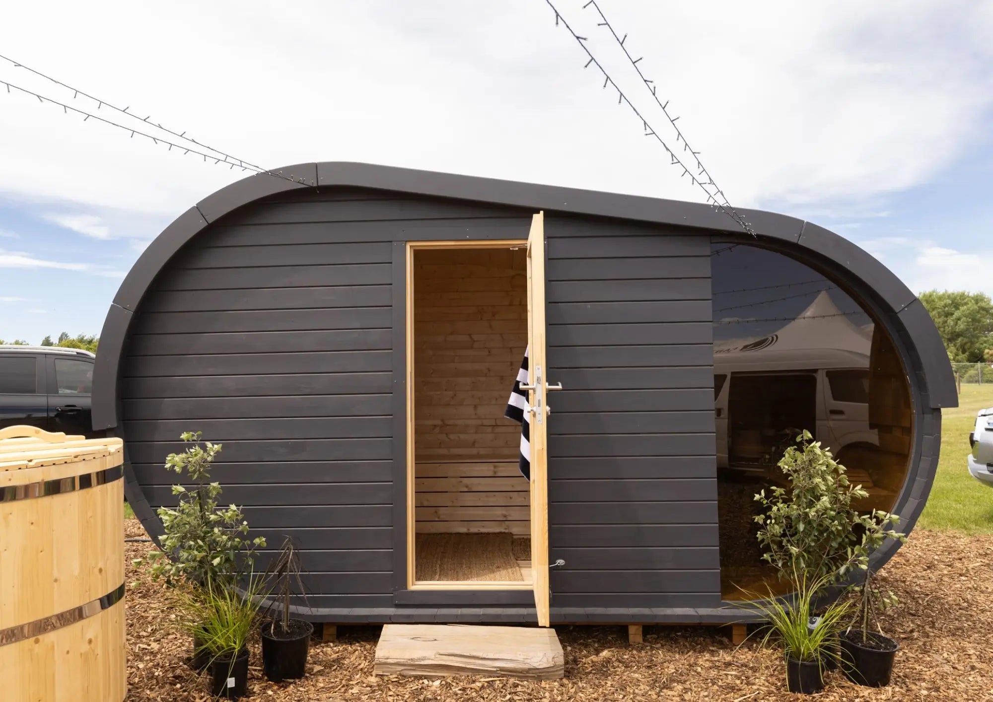 Luxury outdoor sauna building with black cladding, panoramic glass window and timber interior available from GlampLaunch.