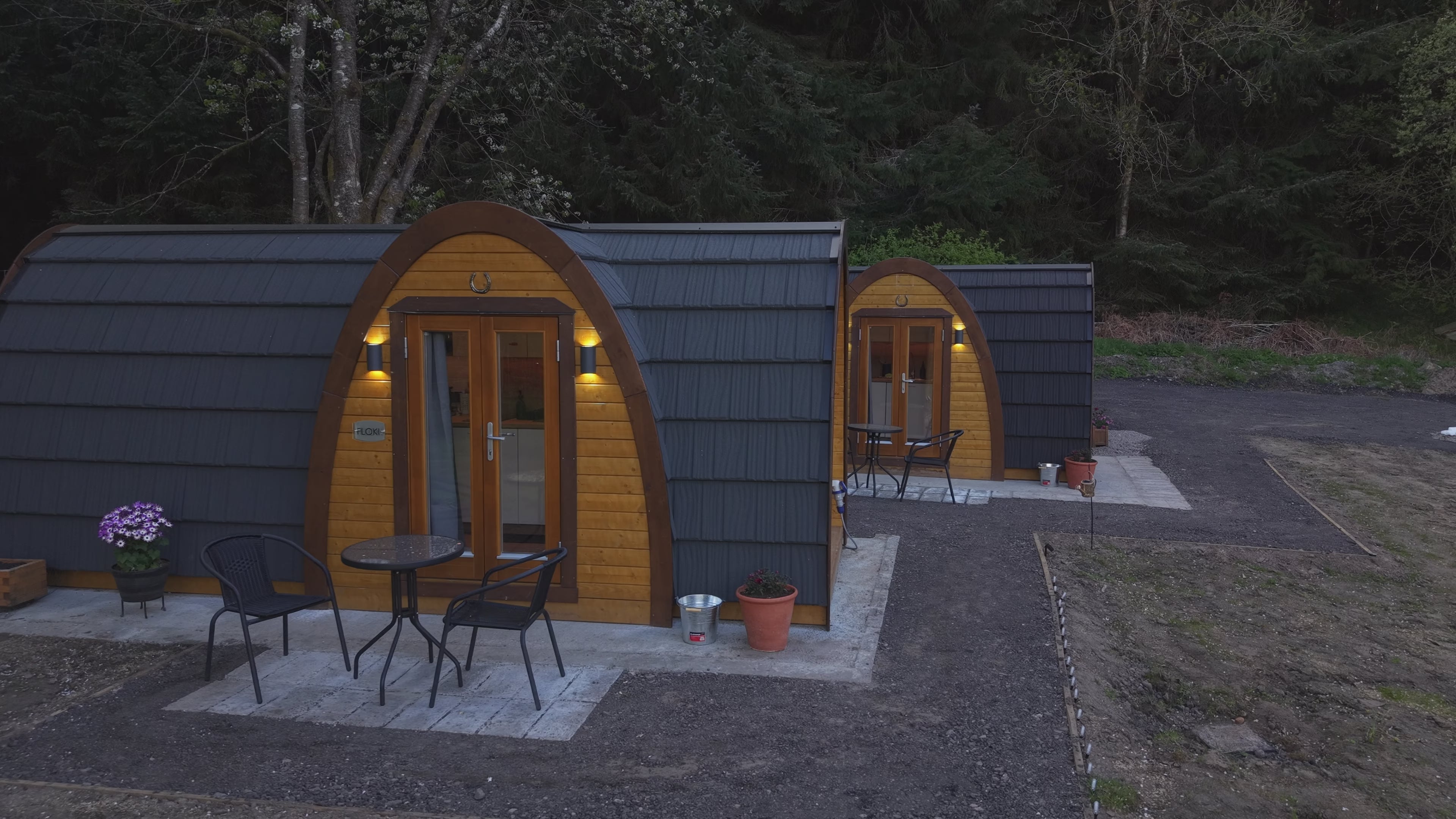 Drone flyout video of two completed glamping pods at Doune House Pods in Scotland, starting with a close aerial view of the accommodation before pulling back to reveal the wider site and surrounding woodland.