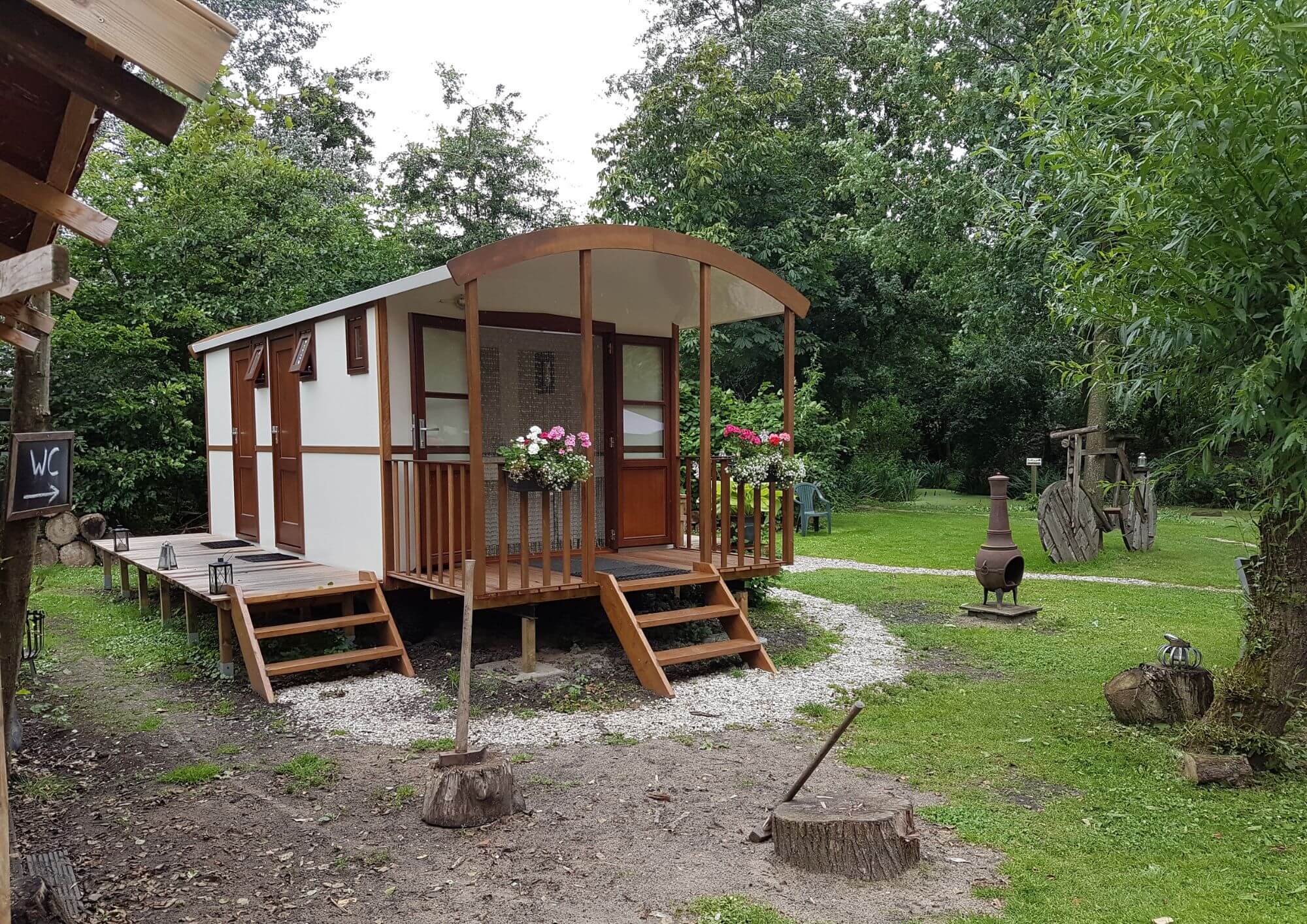 Shepherd's hut converted into a communal WC facility with covered entrance and landscaped surroundings.