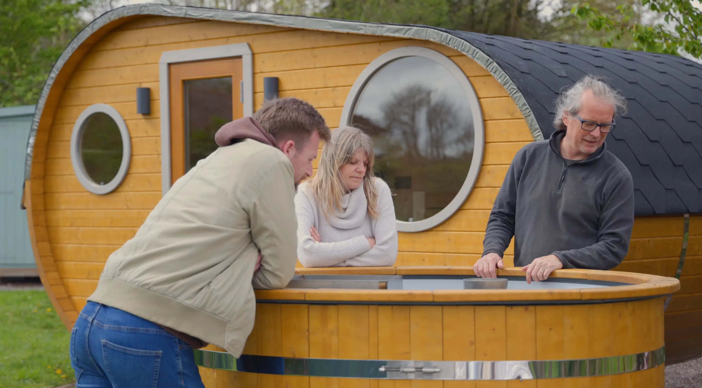Taylor Glass with Steam and Stars owners Jon and Clare Kelly inspecting a hot tub beside their newly delivered GlampLaunch glamping pod during installation day in Somerset.